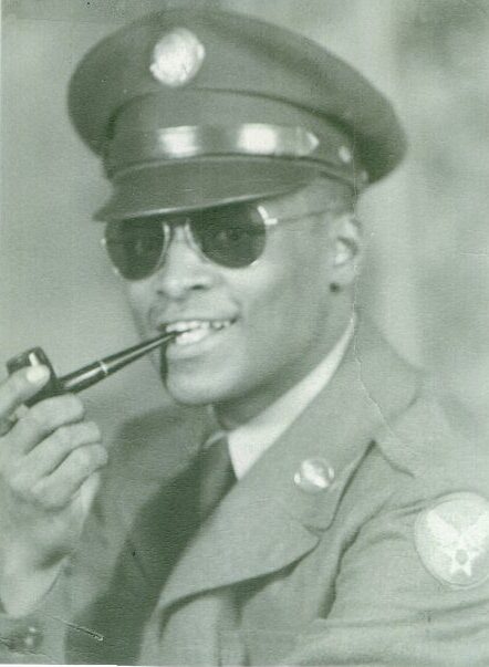 African-American soldier in uniform, holding a pipe, and looking at the camera.